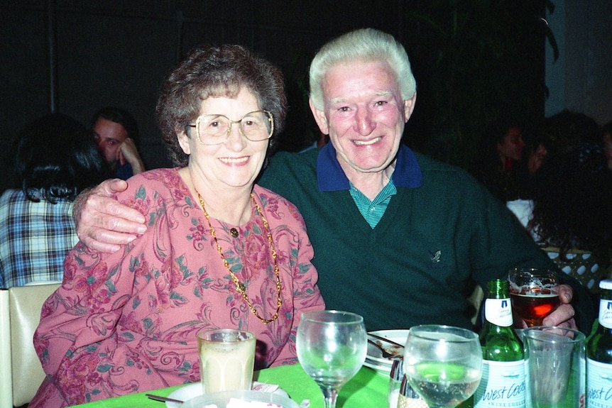 An elderly woman woman and man seated at a table smile for the camera.