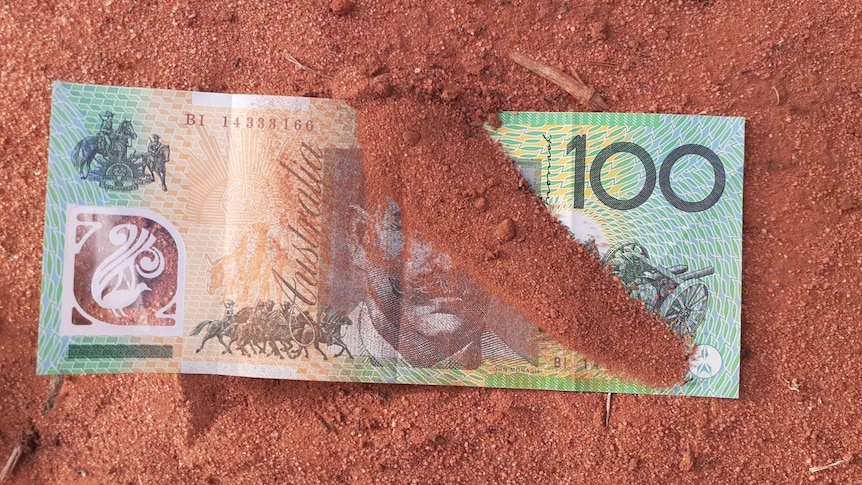 A hundred dollar note in red dirt