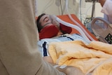 A young man, intubated and with breathing apparatus on, in a hospital bed.