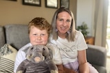 a young boy with red hair and his mother with blonde hair sit on a couch.