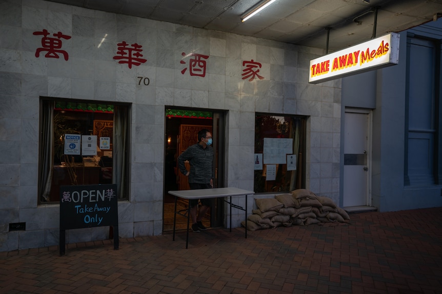 A man looking out from a shop front with sandbags beside him