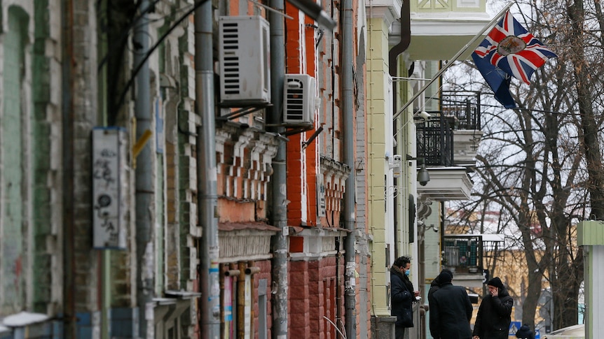 People gather on a street in Kyiv in front of a building flying a British flag