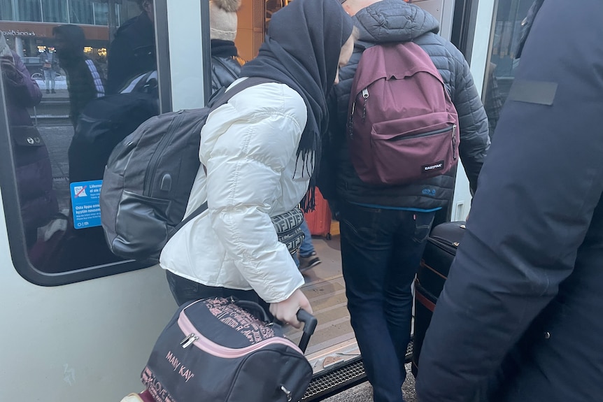 Женщина с черным платком на голове садится в поезд вместе с другими.