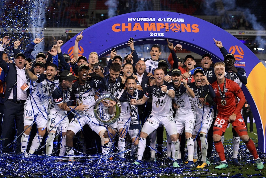 Melbourne Victory players celebrate their win over the Jets with the A-League trophy.