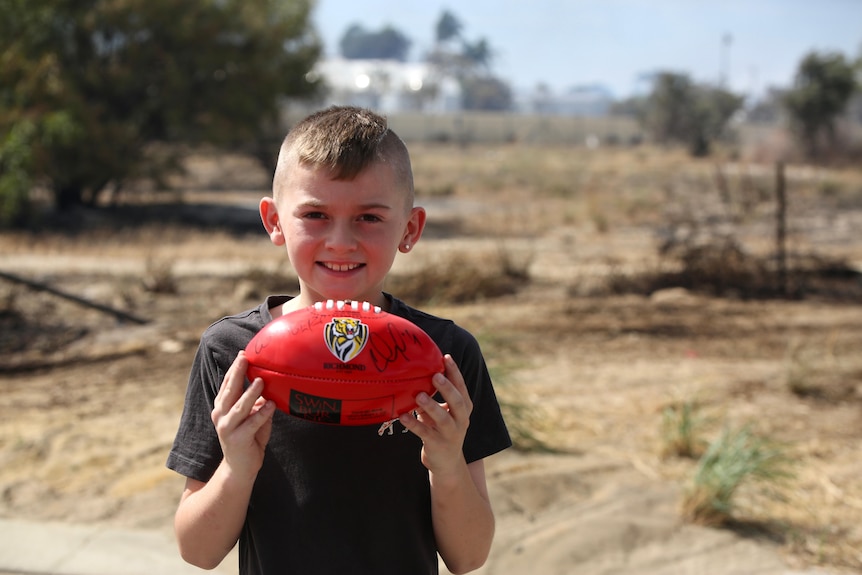 A smiling boy holds up a red football