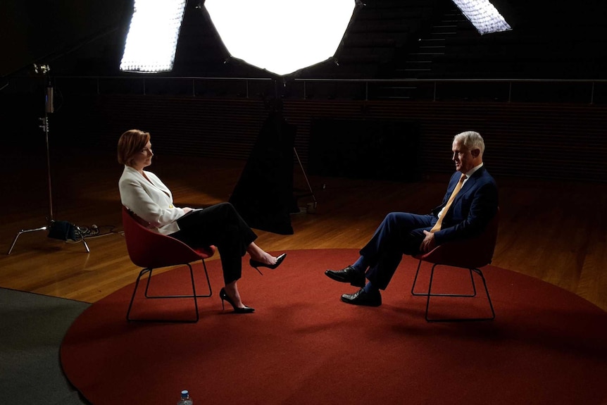 Malcolm Turnbull and Leigh Sales sitting on separate chairs facing each other with bright lights in the background