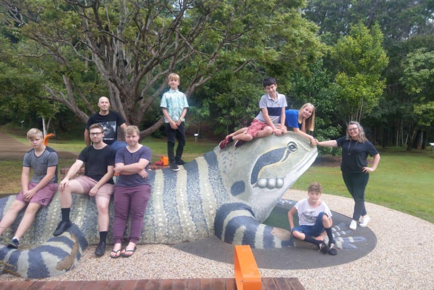Dawn and husband with their 7 children sitting on and around at the Giant Lizard stature in the park in Port Macquarie.