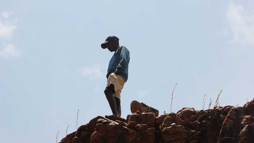 Silhouette of a young man standing on a rock face looking out