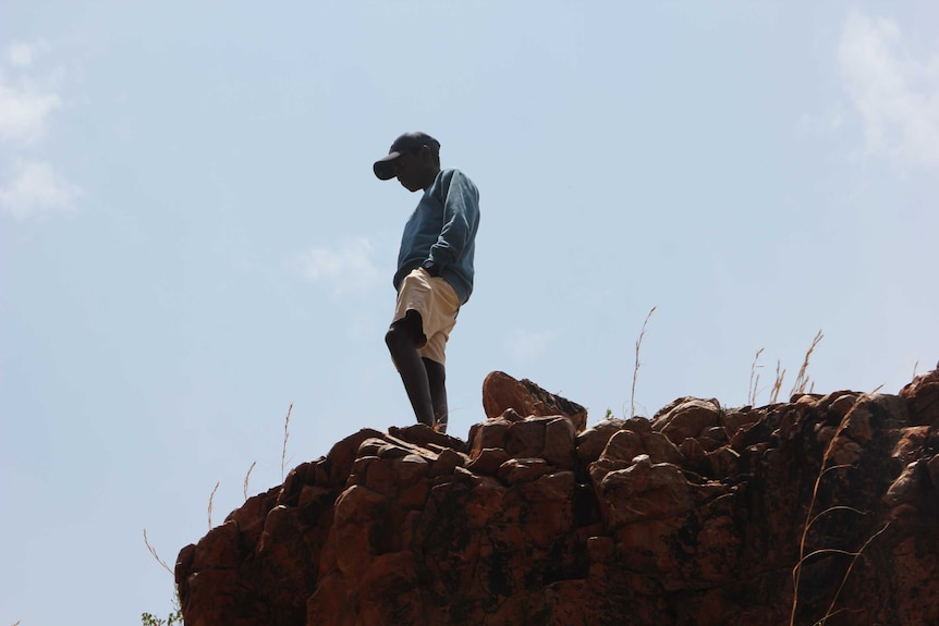 Silhouette of a young man standing on a rock face looking out