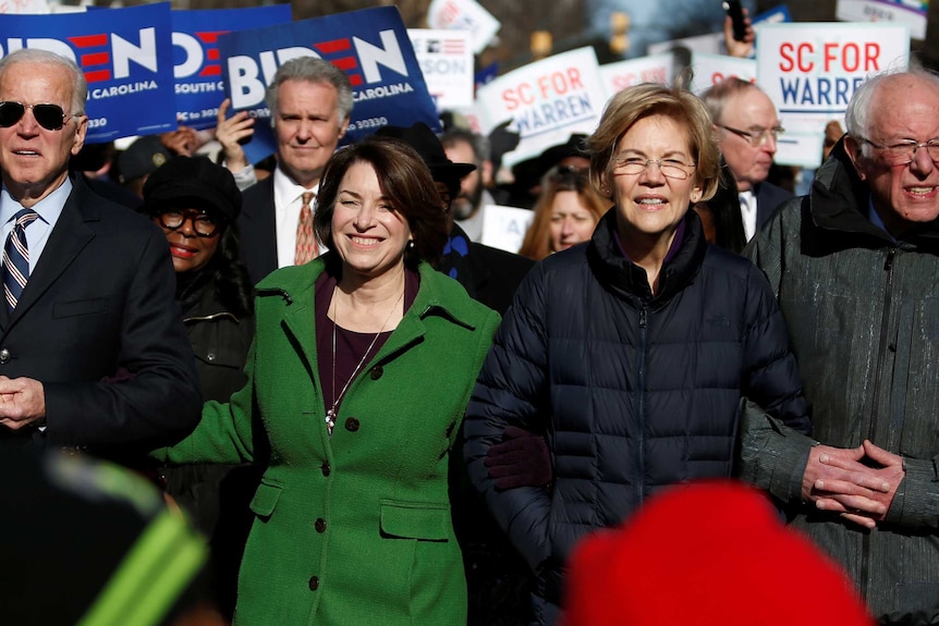 Joe Biden, Amy Klobuchar, Elizabeth Warren and Bernie Sanders walking arm in arm