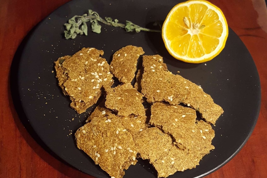 A black plate with yellow crackers on it with a cut lemon