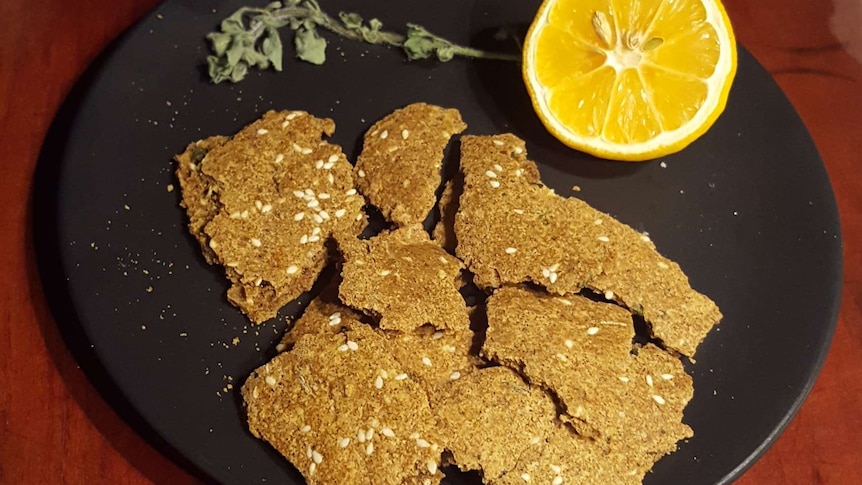 A black plate with yellow crackers on it with a cut lemon