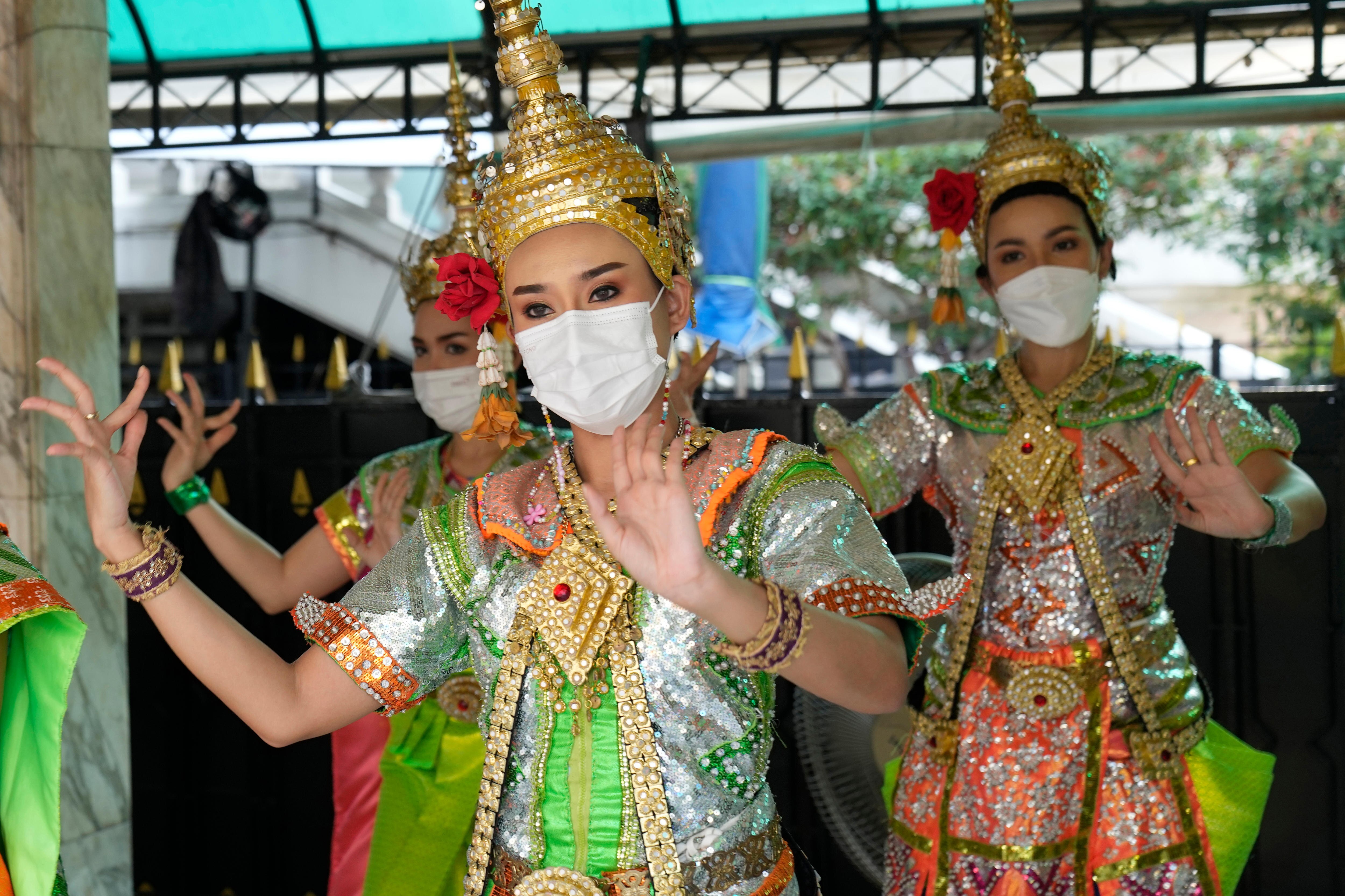 Thai traditional dancers in gold headresses wear masks and do hand gestures