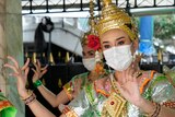 Thai traditional dancers in gold headresses wear masks and do hand gestures
