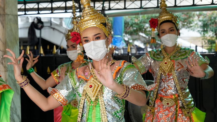 Thai traditional dancers in gold headresses wear masks and do hand gestures