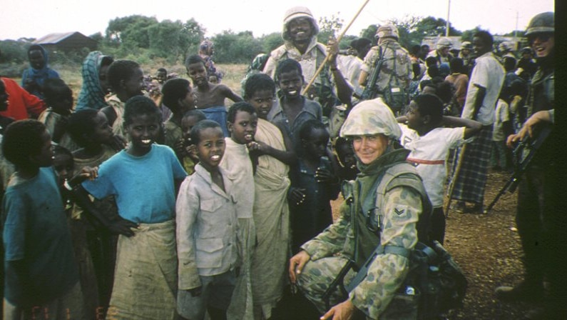 Wayne Douglas, dressed in his Army uniform, poses for a photo with children at a refugee camp in Somalia.