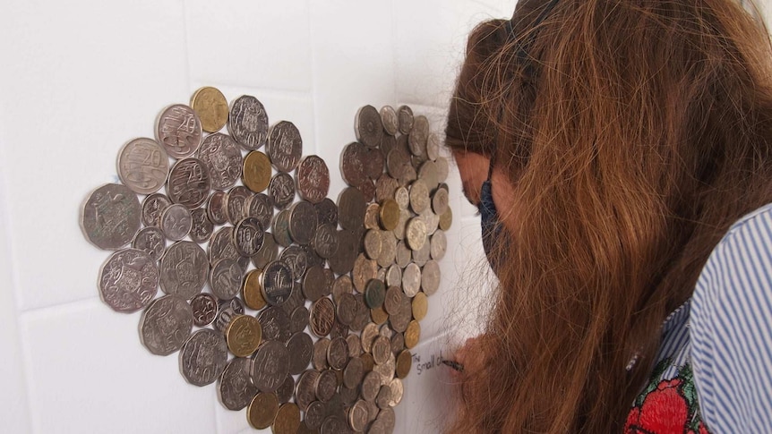Close up headshot of  Laura Cantrill writing The Small Change Project on a wall, that has coins stuck on it, in a heart shape