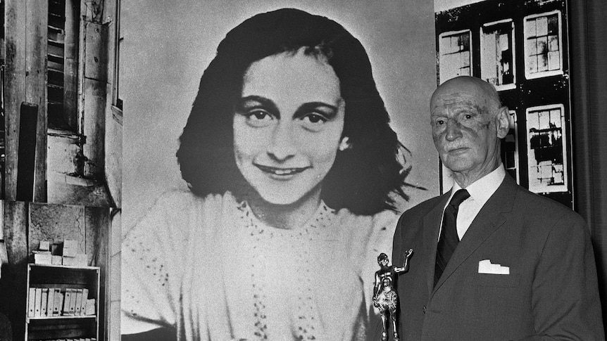 Otto Frank stands beside a large photo of his daughter Anne Frank