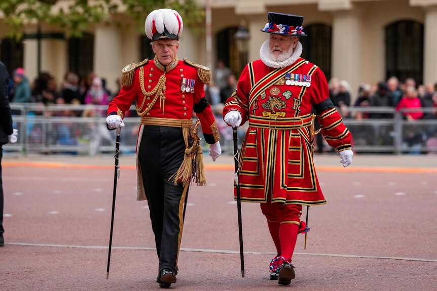 Two men in British regalia walk past a policeman. 