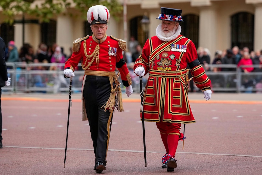 Two men in British regalia walk past a policeman. 