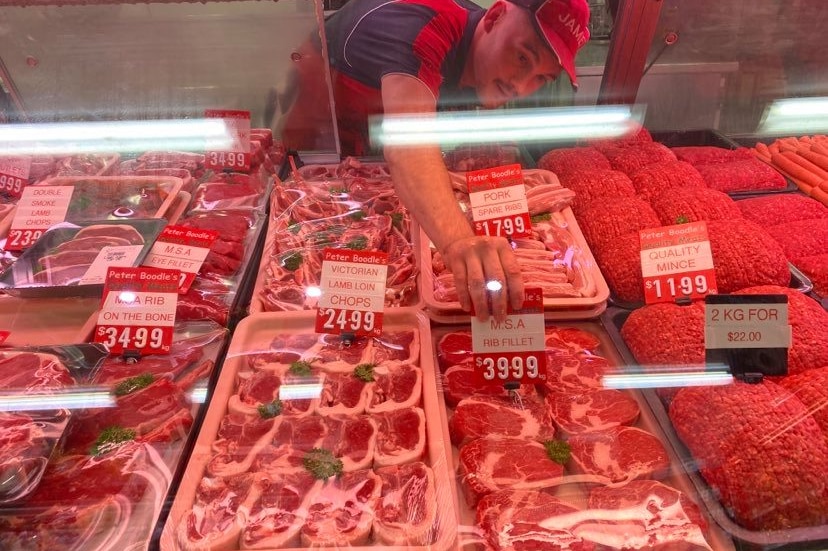 A man puts a label on steak in the deli window.