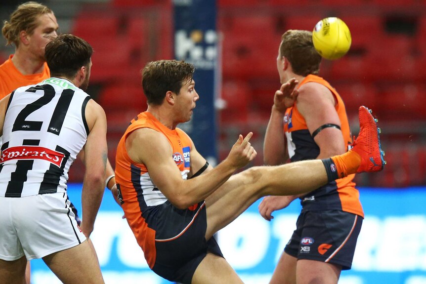 An AFL player hooks the ball towards goal with his right foot, as other players look on.