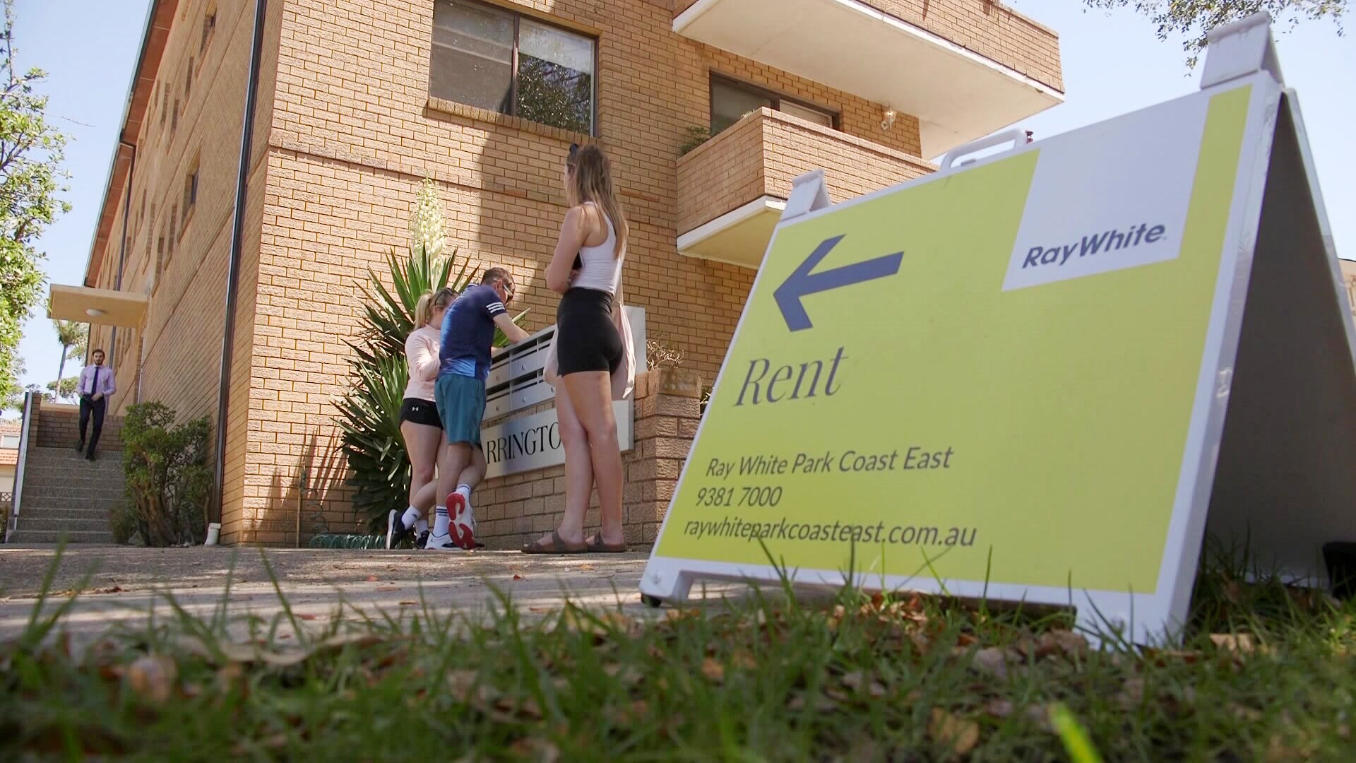 Rent sign outside apartment inspection site with people lining up