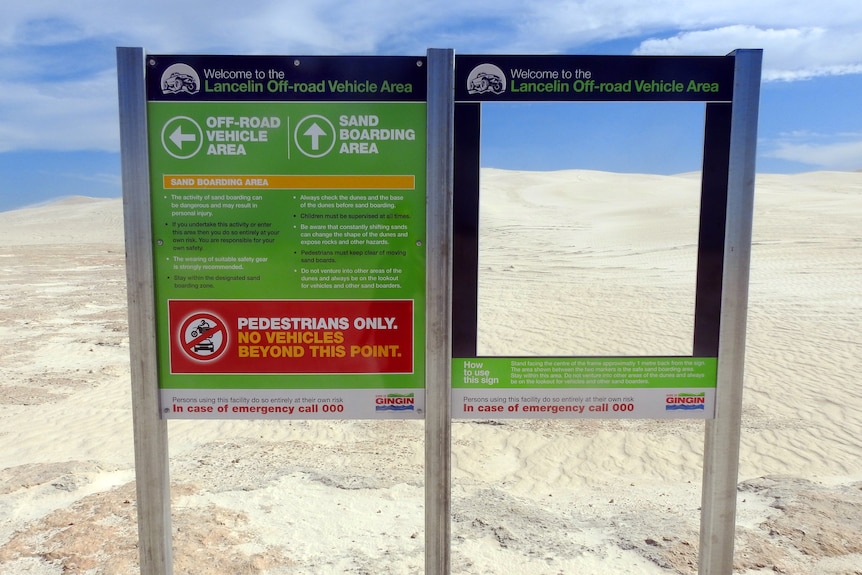 Signs in front on white sand dunes.