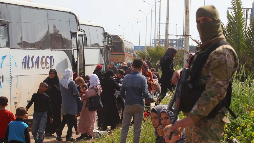 A rebel fighter stands near buses.