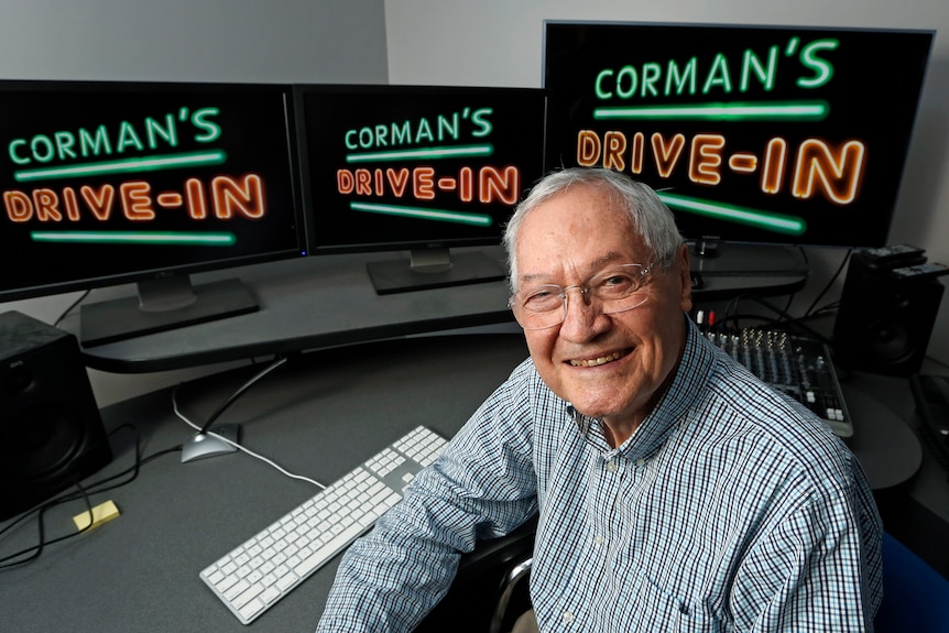 A man sitting in front of three computer monitors with the words "corman's drive-in" 