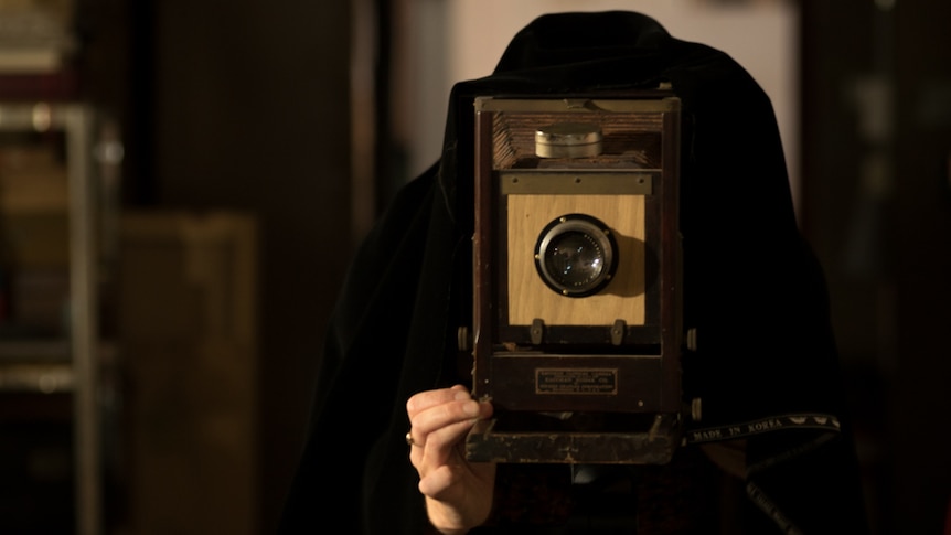Aurelia Carbone adjusts a tintype camera while underneath its the cloak.