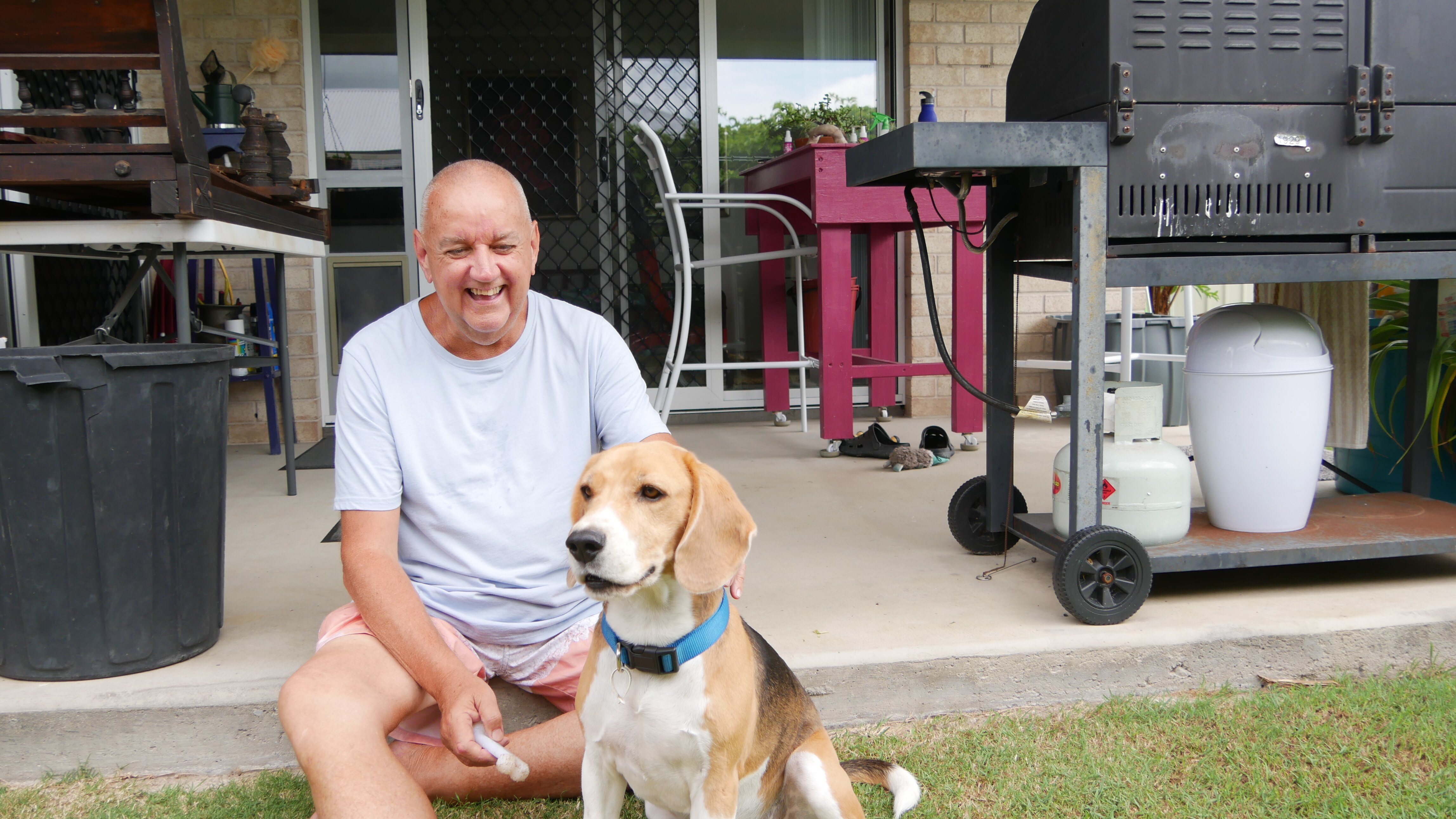 A man laughs at his dog while sitting on a patio.