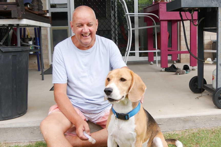 A man laughs at his dog while sitting on a patio.