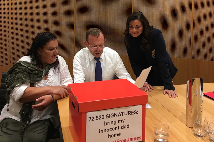 Tony Abbott reads over a piece of paper with two women watching on