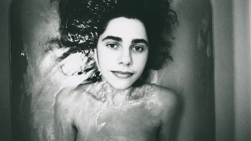 Black and white photo of PJ Harvey lying face-up in a bath of water