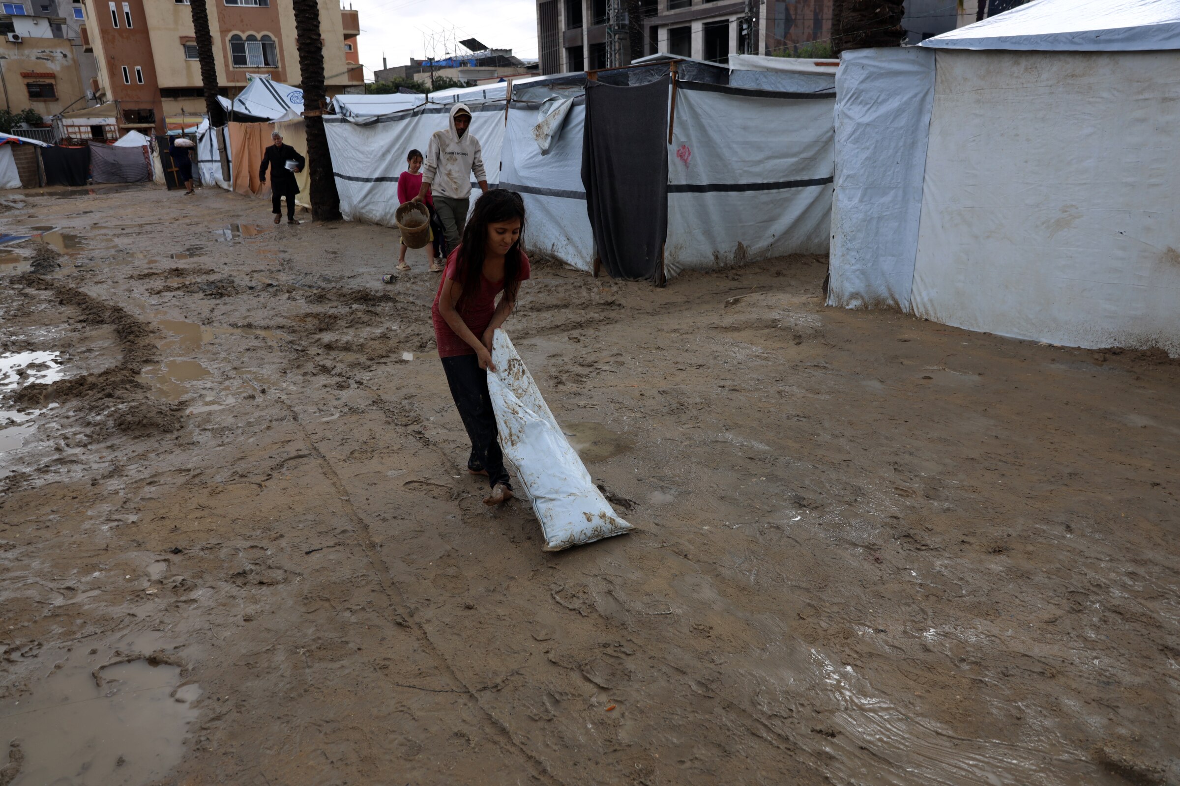 A young girl pulling a bag along muddy ground with tents lining the area.