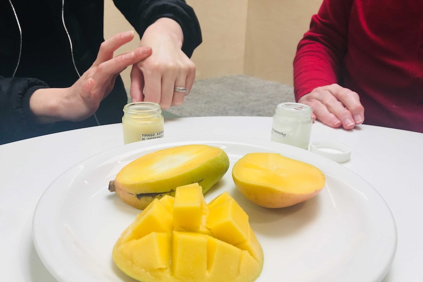 A close of of a woman's hands having moisturiser applied while there is an open mango in the foreground.