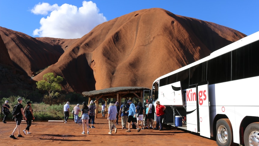 Tourists exit a bus at the base of Uluru.