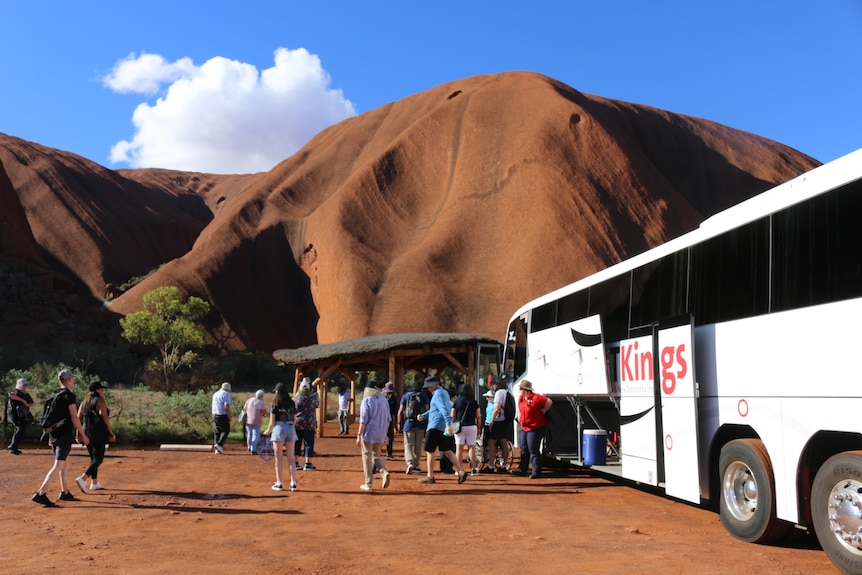 Tourists exit a bus at the base of Uluru.