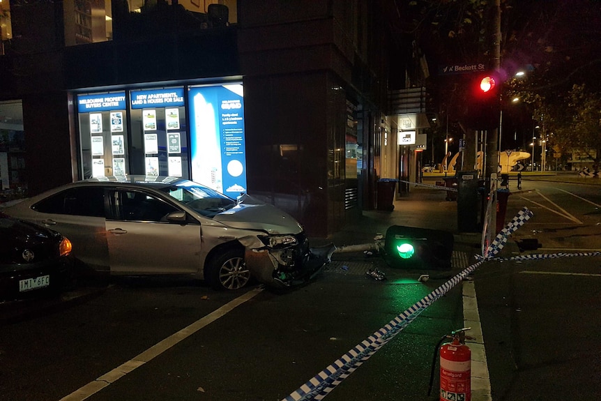 A damaged car with a stop light under its front bumper.