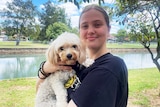 a young woman holding onto a dog outside at a park