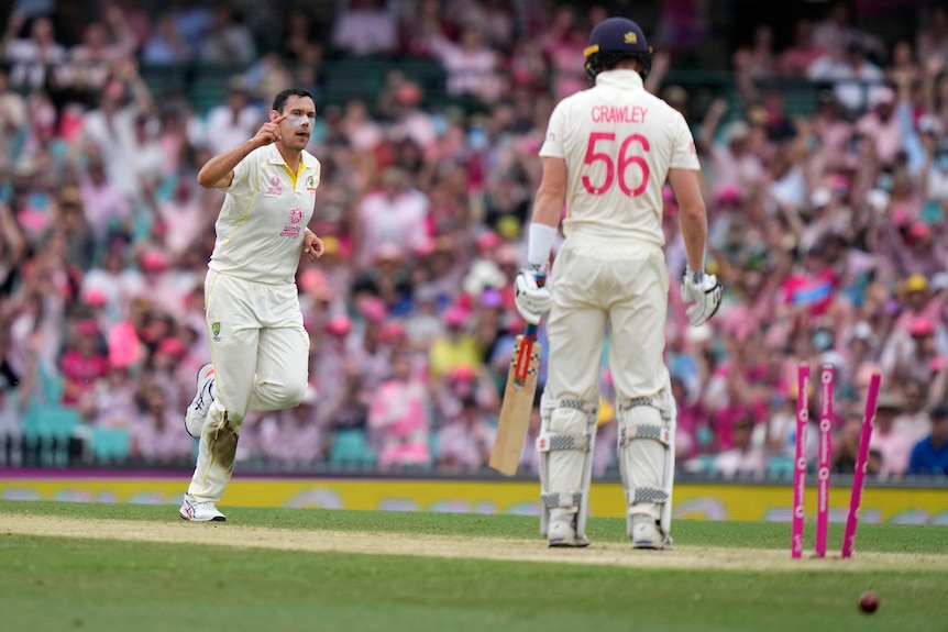 Australia bowler Scott Boland puts his hand in the air as England batter Zak Crawley stands in front of broken stumps.