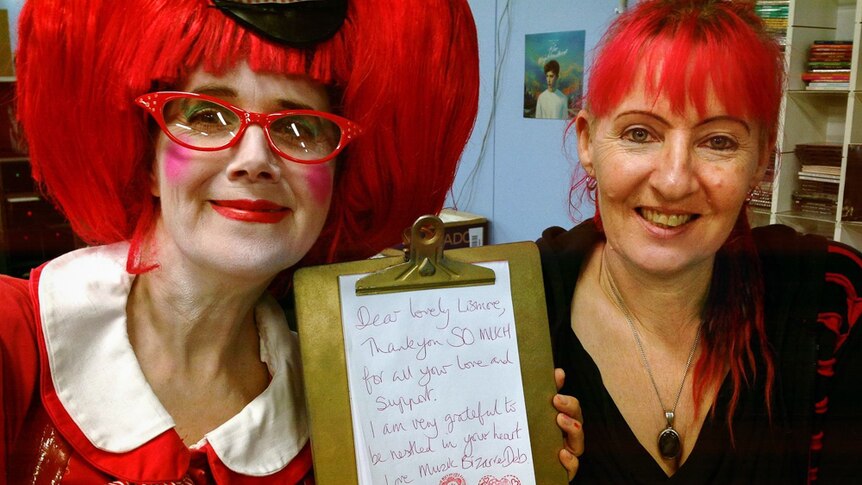Two women with red hair holding a note that has a thank you message on it to the Lismore community.