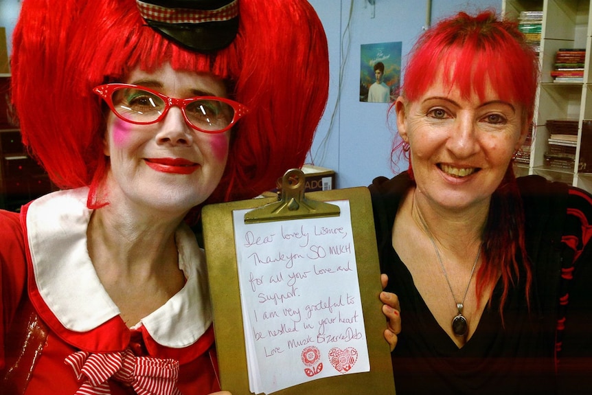 Two women with red hair holding a note that has a thank you message on it to the Lismore community.