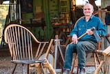 Man with axe sitting on Windsor-style wooden armchair.