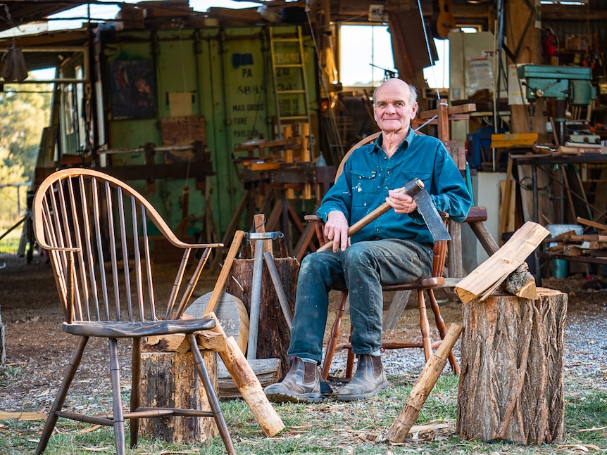 Man with axe sitting on Windsor-style wooden armchair.