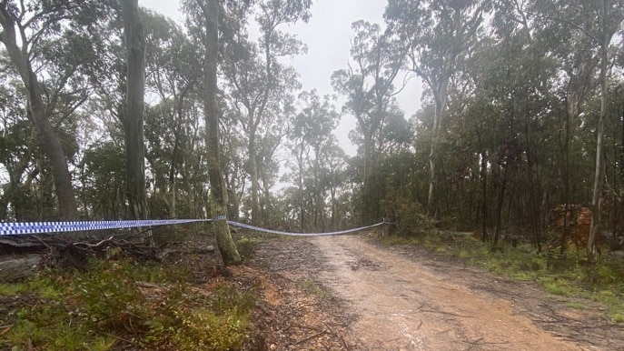 Some police tape is hung between trees on a wet, muddy unsealed road