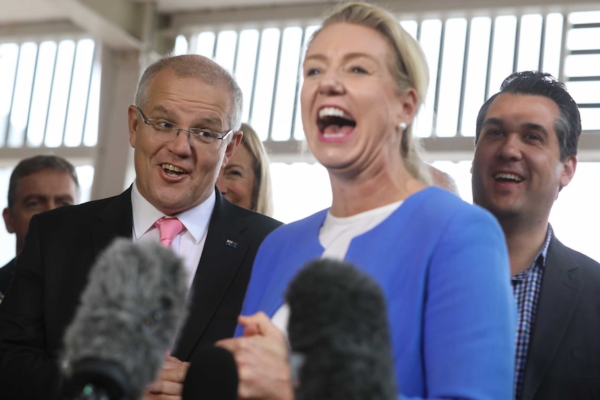 Morrison and McKenzie are laughing at a press conference, standing in front of microphones and Liberal Michael Sukkar.