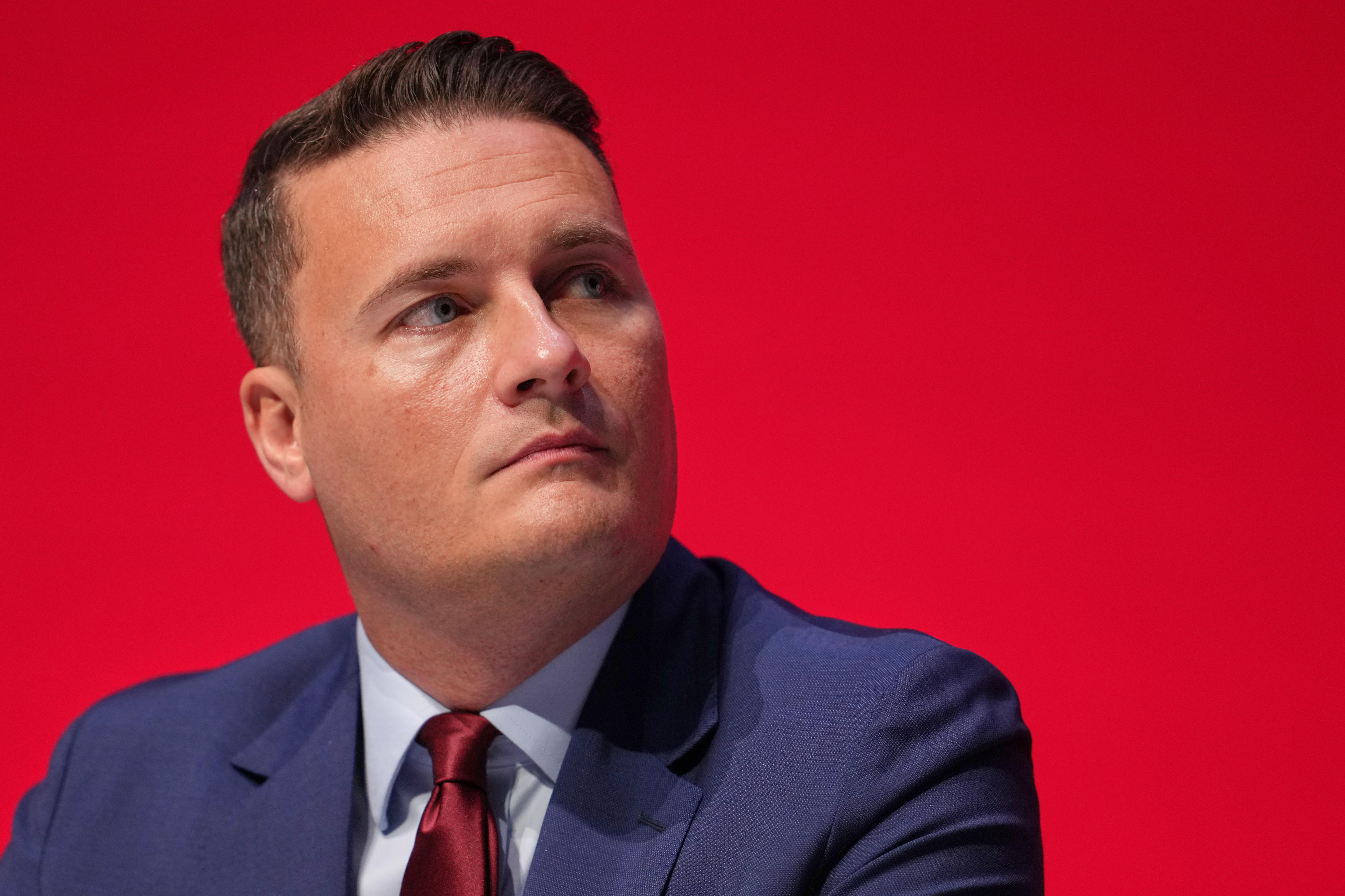 Wes Streeting olhando para cima e para a esquerda na frente de um fundo vermelho.