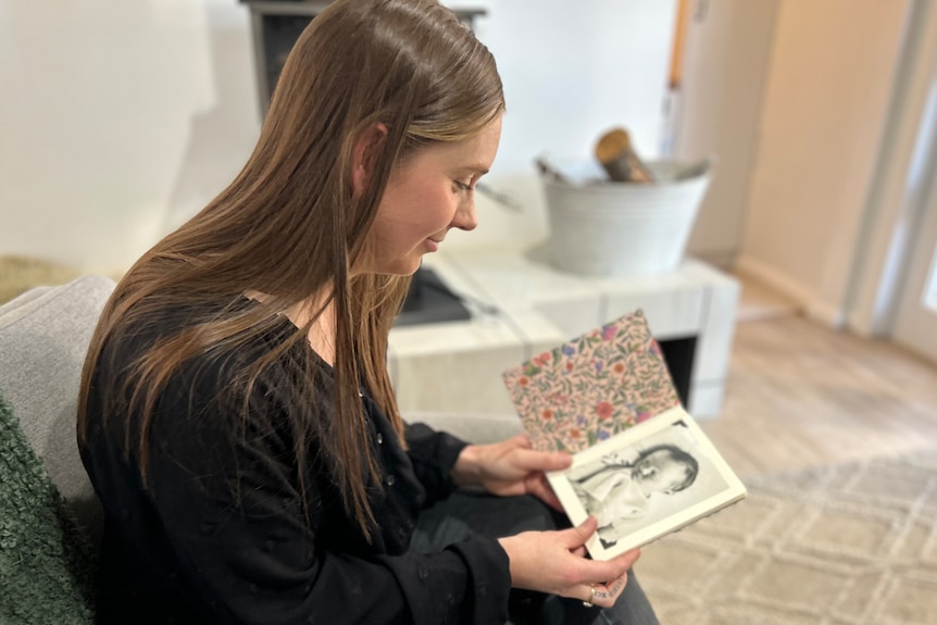 A woman sitting on a couch looks lovingly at a photo album of a baby